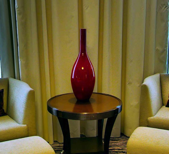 Red glass vase on a side table between two armchairs